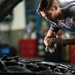 Young,mechanic,wiping,his,hands,while,repairing,car,engine,in